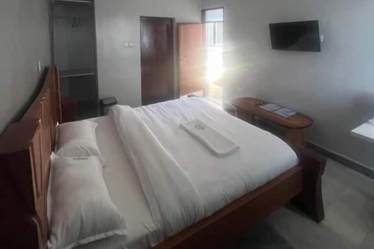 Quarto de hotel com cama, escrivaninha, televisão e guarda-roupa.