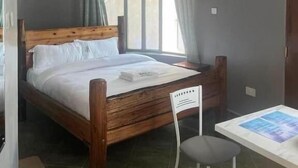 A bedroom with a wooden bed, a desk with a chair, and a window with curtains. - Oleng'oti Gardens Narok (Narok)
