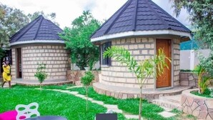 Two small, round, brick-roofed structures with a stone base, surrounded by a well-maintained garden with a paved path. - Oleng'oti Gardens Narok (Narok)
