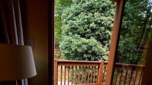 A wooden deck with a railing, a door leading to an outdoor area, and a lamp on the left.