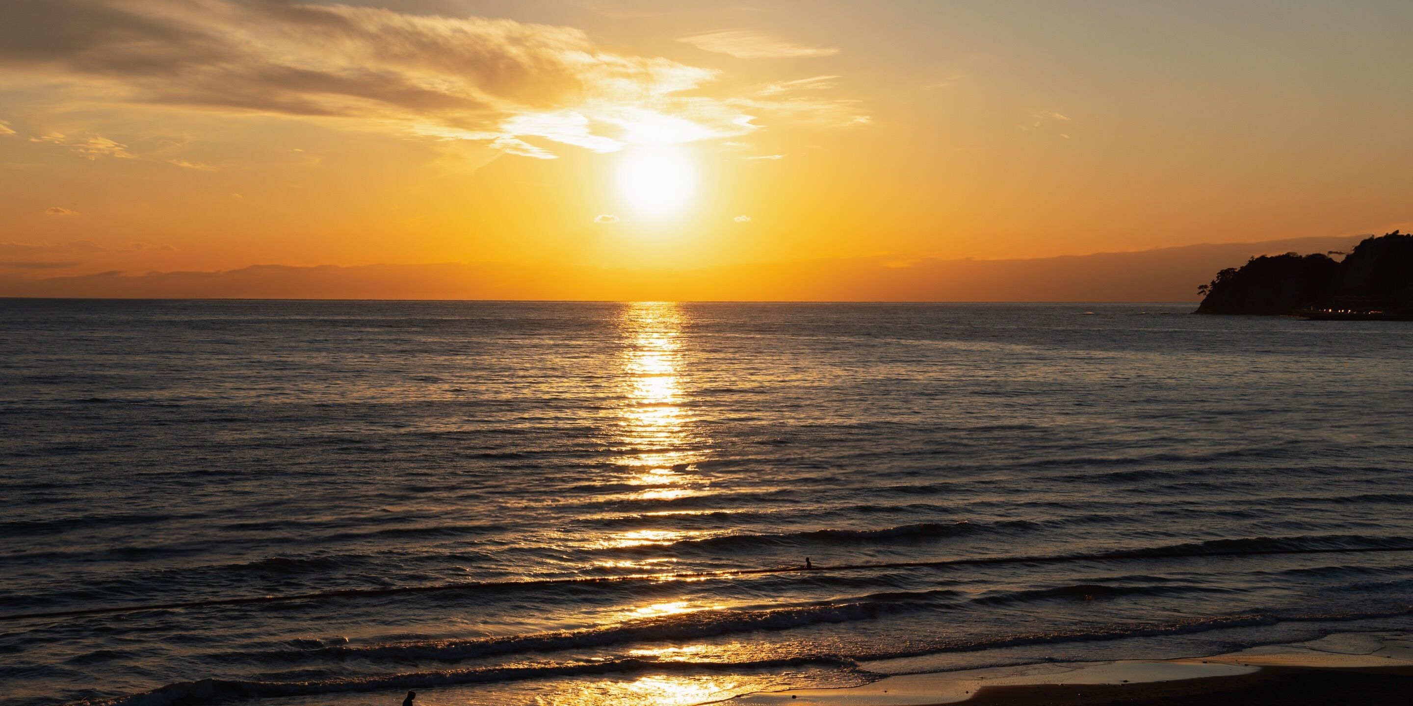 Un coucher de soleil sur une mer calme, avec une terre lointaine à l’horizon.