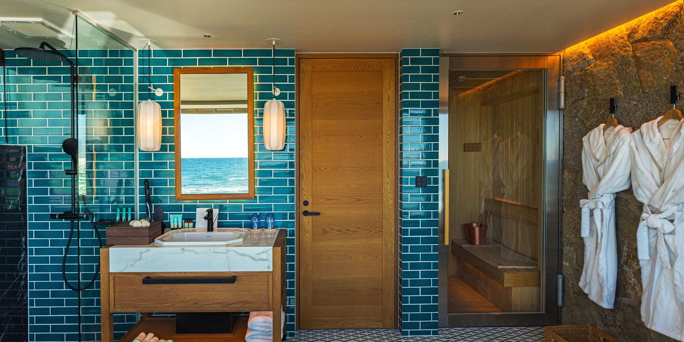 A bathroom with a large mirror, a sink, and a shower. There are towels and toiletries on the counter.