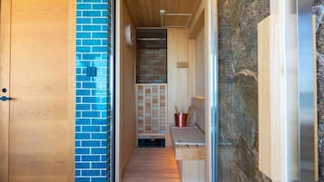 A hallway with a wooden door, a blue-tiled wall, a sauna area with a bench, and a stone wall.