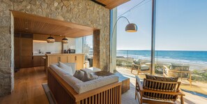 A modern living room with a stone wall, wooden furniture, and a view of the beach. - UMITO VILLA KAMAKURA ZAIMOKUZA (Kamakura)