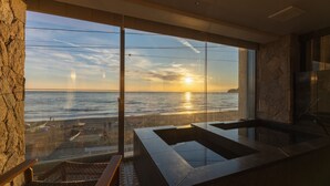 Un baño moderno con un amplio ventanal con vistas a una playa al atardecer.