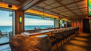 A modern bar with a long counter, multiple chairs, and a large window overlooking the sea. - UMITO ATAMI BETTEI (Atami)