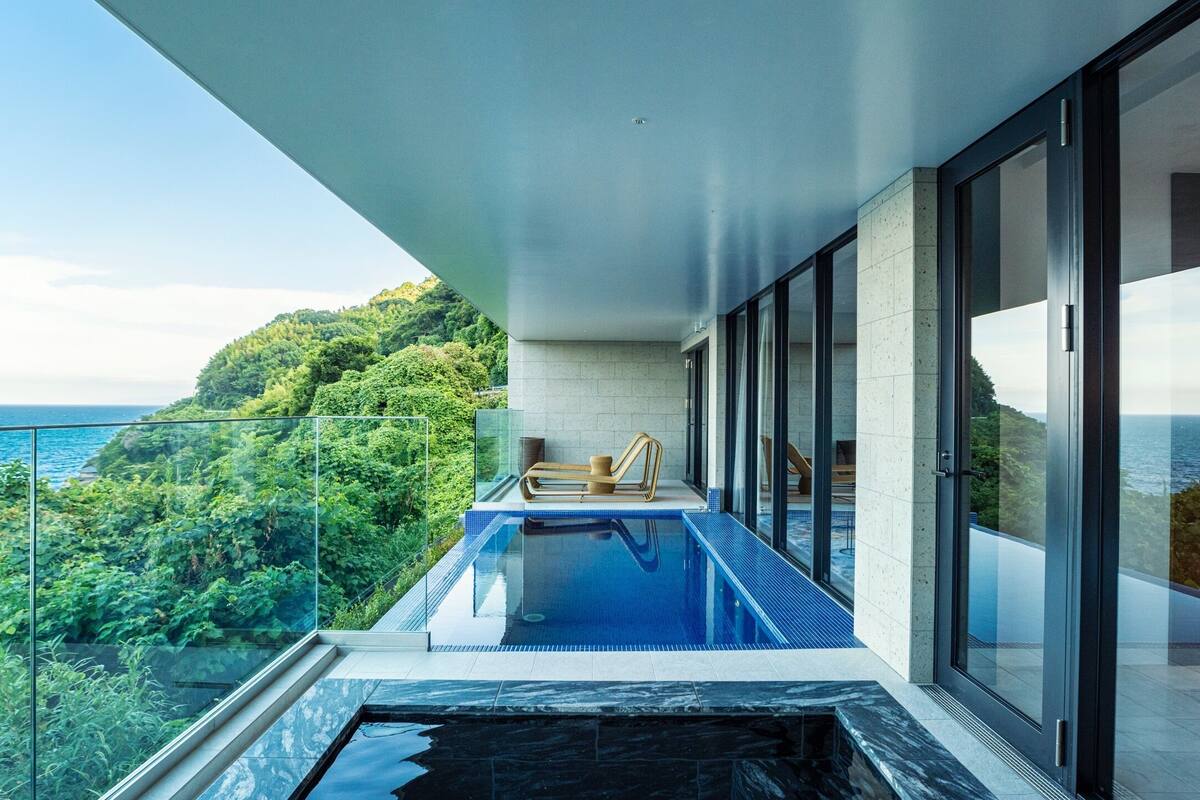 A modern infinity pool with a clear view of the ocean and lush greenery.