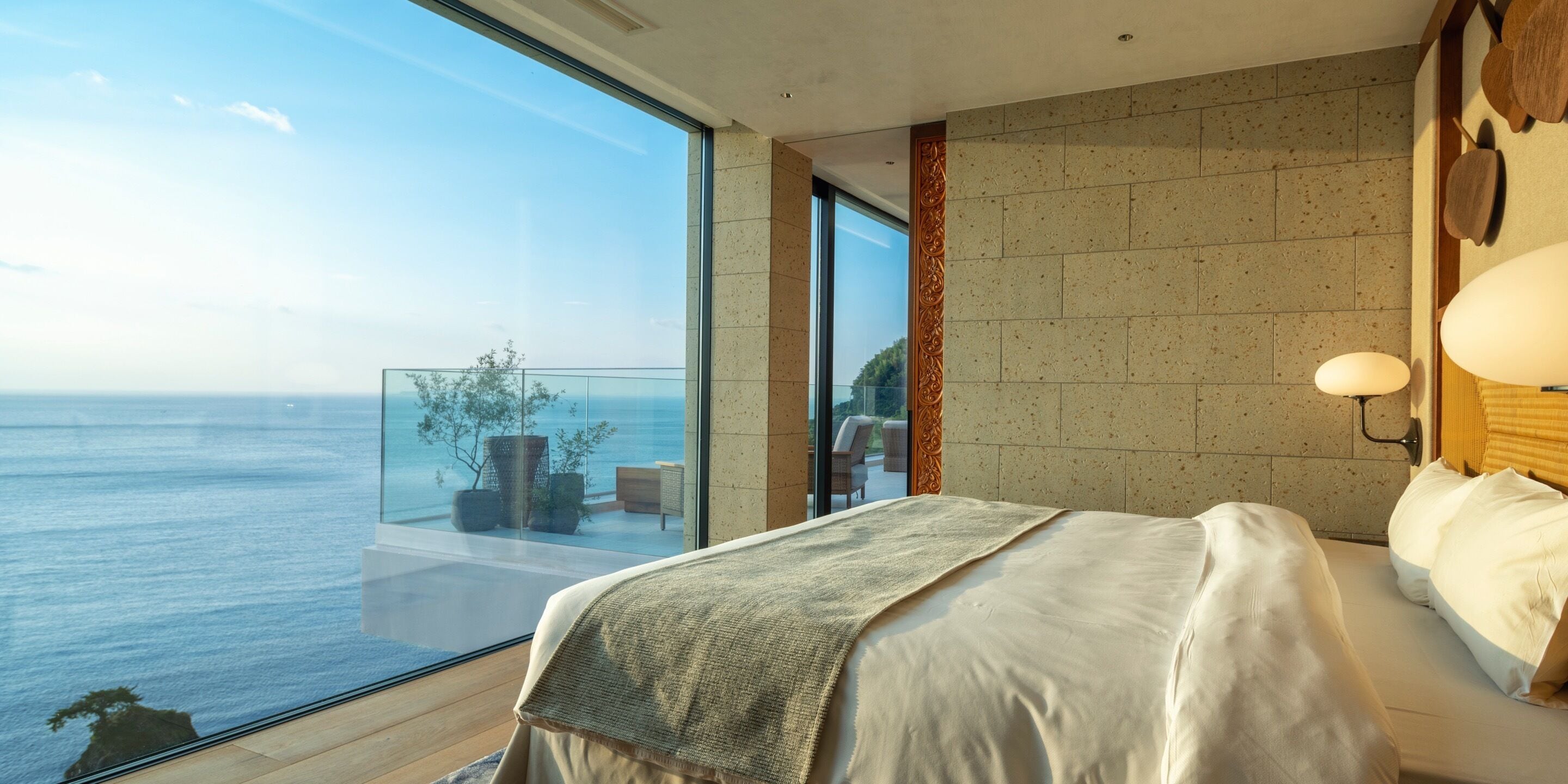 A modern hotel room with a large bed, a view of the sea, and a balcony with outdoor furniture.