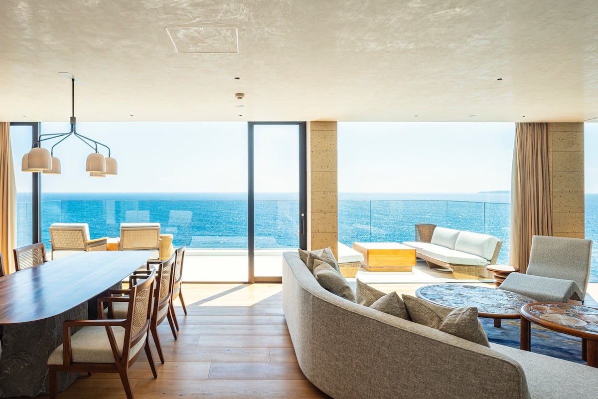 A modern living room with a large wooden dining table, comfortable seating, and a view of the ocean.