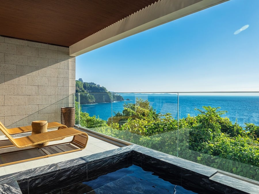 A balcony with a view of the sea, a hot tub, and wicker furniture.