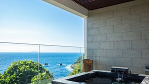 A modern bathroom with a large window overlooking the ocean, a hot tub, and a stone wall. - UMITO ATAMI BETTEI (Atami)