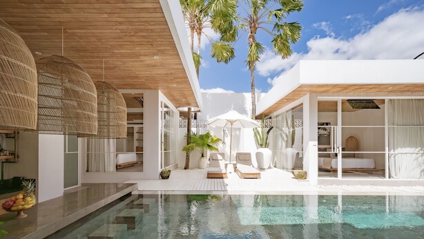 A modern pool area with clear water, white furniture, and tropical plants.