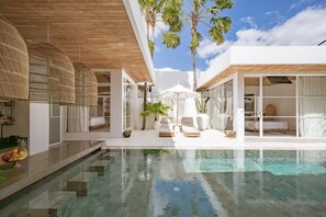 Un área de piscina moderna con agua cristalina, muebles blancos y plantas tropicales.