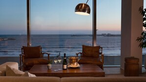 A room with a large window overlooking the ocean, two wooden chairs, a wooden table with a bottle and glasses, and a hanging light fixture. - UMITO KAMAKURA KOSHIGOE (Kamakura)