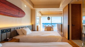 A modern hotel room with a large bed, a wooden headboard, a surfboard on the wall, and a view of the ocean through large windows. - UMITO KAMAKURA KOSHIGOE (Kamakura)