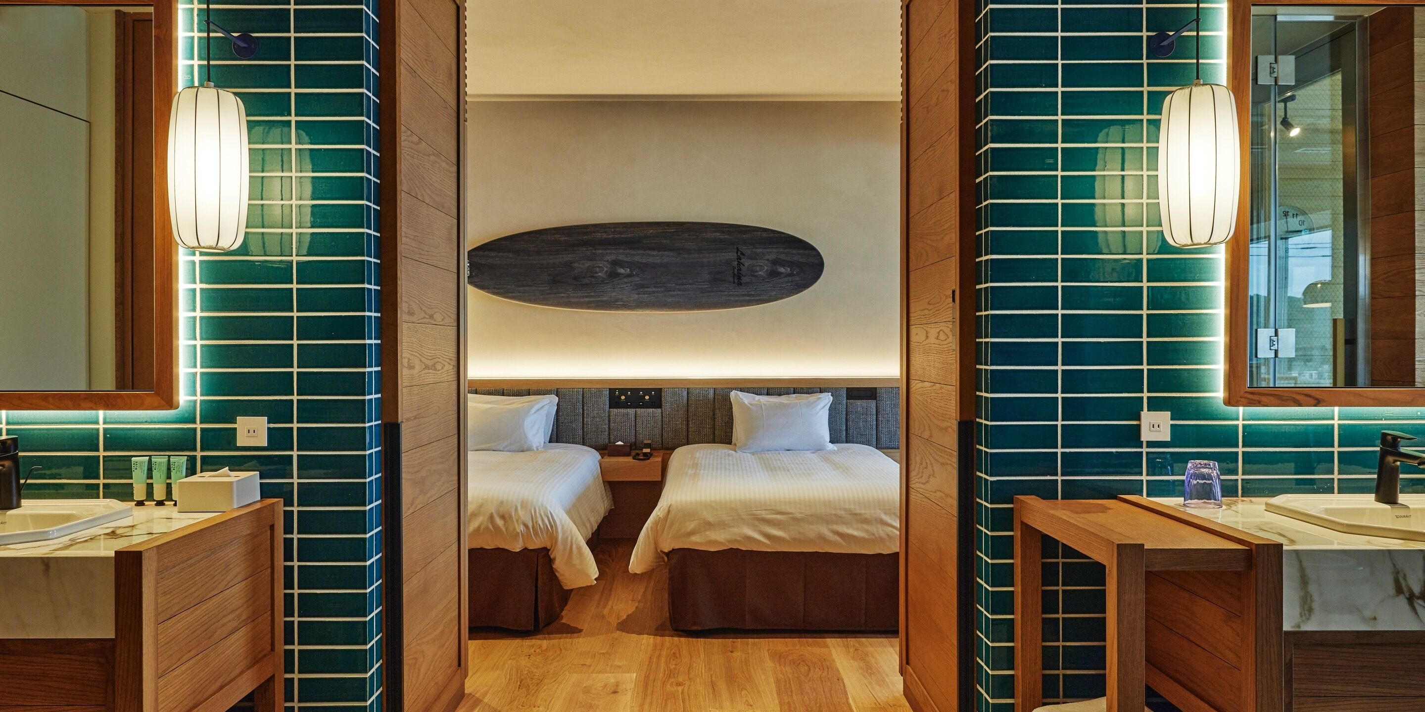 Quarto de hotel com duas camas, cabeceira de madeira, espelho grande e toucador de madeira com pia.