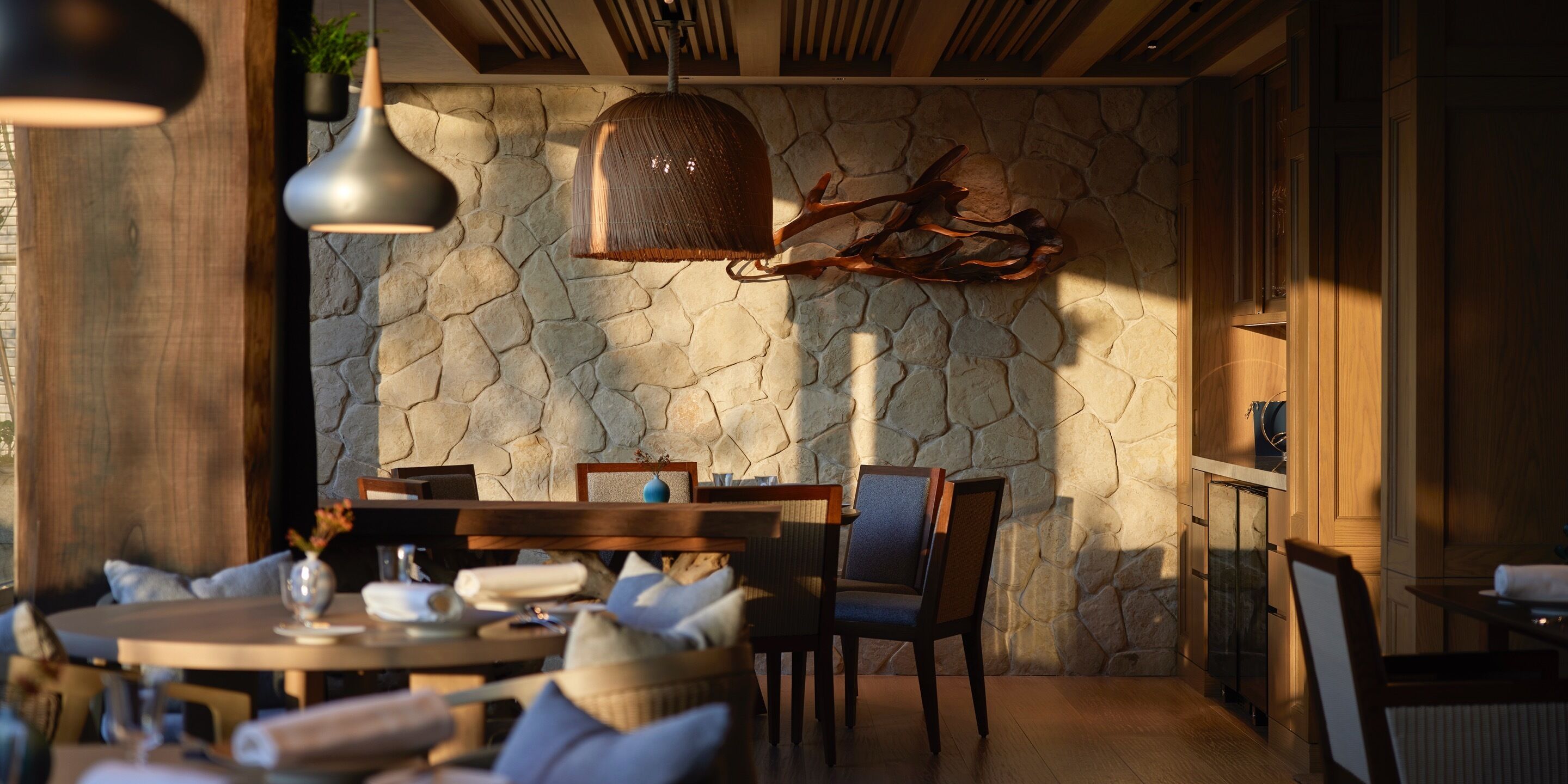 A dining area with a stone wall, wooden furniture, and pendant lighting.