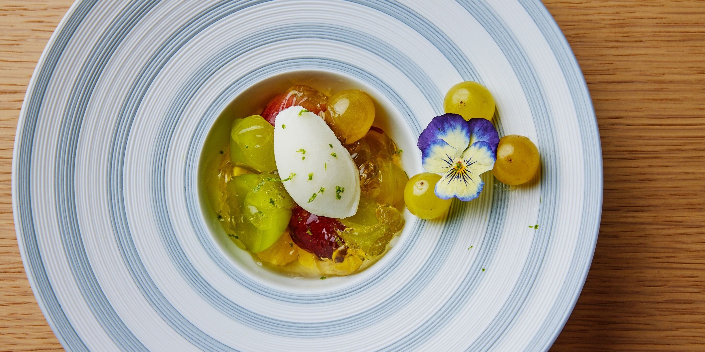 Uma fatia de sobremesa com fruta e uma colherada de creme, decorada com uma flor.
