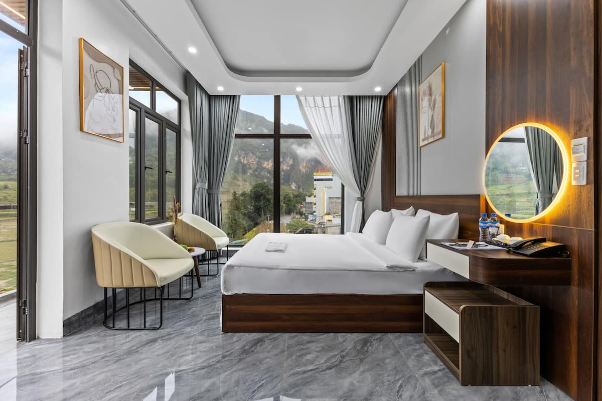 Quarto de hotel moderno com uma cama grande, uma escrivaninha, uma cadeira e vista para as montanhas.