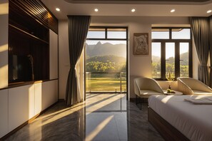 Ein modernes Hotelzimmer mit einem großen Bett, zwei Sesseln, einem kleinen Tisch und einem Balkon mit Bergblick.