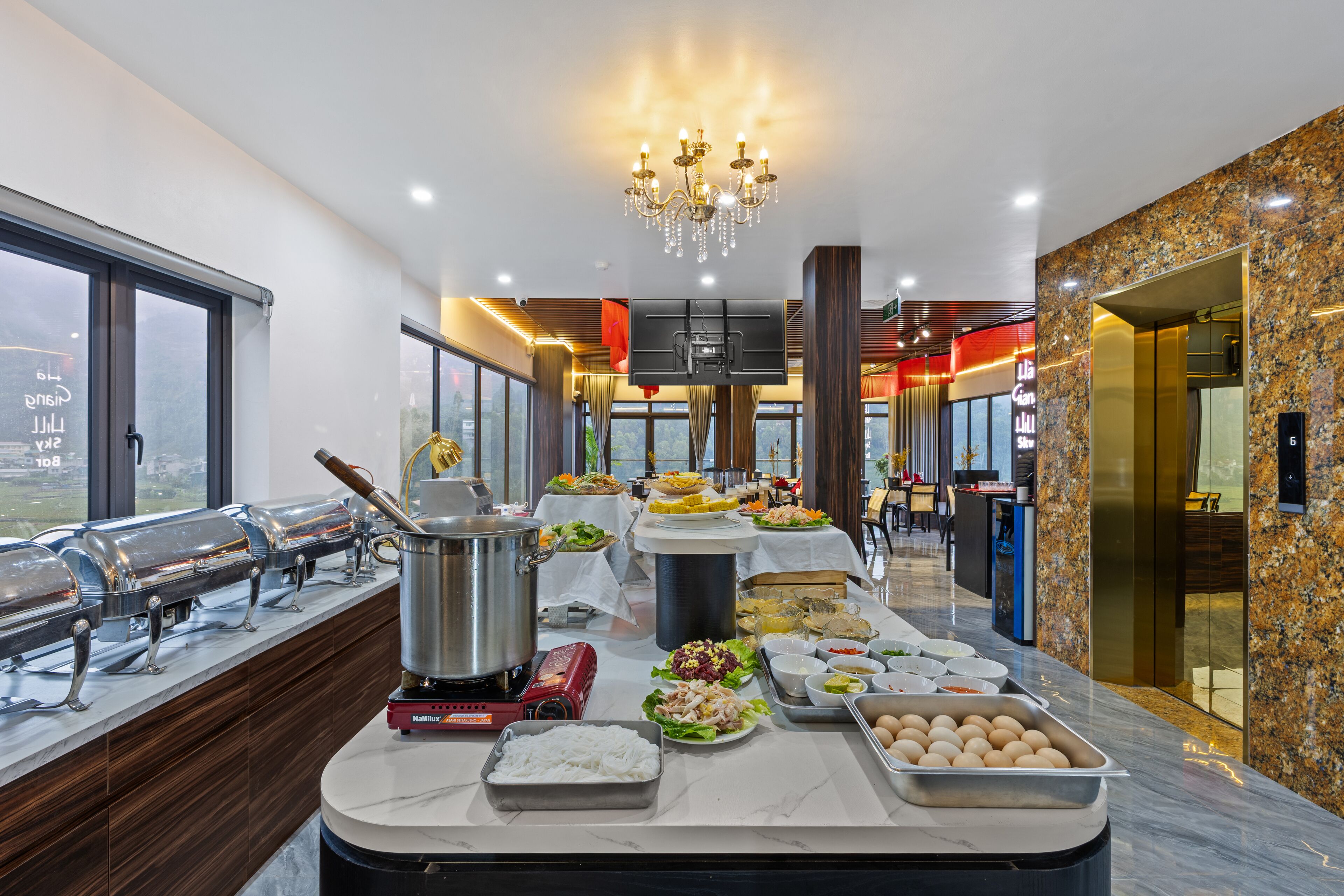 A buffet setup with various food items, a large pot, and a red appliance on a marble countertop.