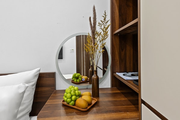 Ein ordentlich eingerichtetes Zimmer mit Nachttisch aus Holz, einem Spiegel und einer Vase mit Trockenpflanzen.