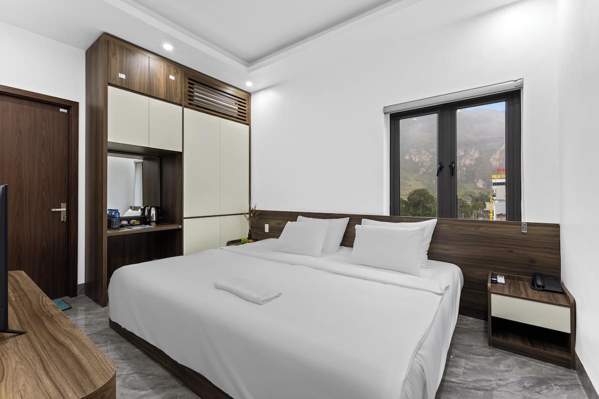 Quarto de hotel moderno com uma cama grande, um guarda-roupa de madeira, uma escrivaninha e uma janela com vista para as montanhas.