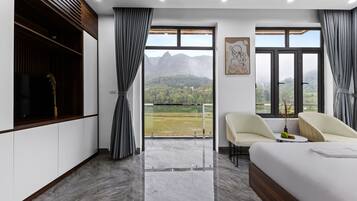 Habitación de hotel moderna con una cama grande, dos sillas, una mesita y un balcón con vistas a la montaña.