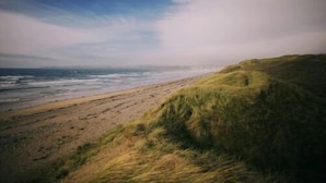 Una playa con una duna cubierta de hierba y el océano al fondo.