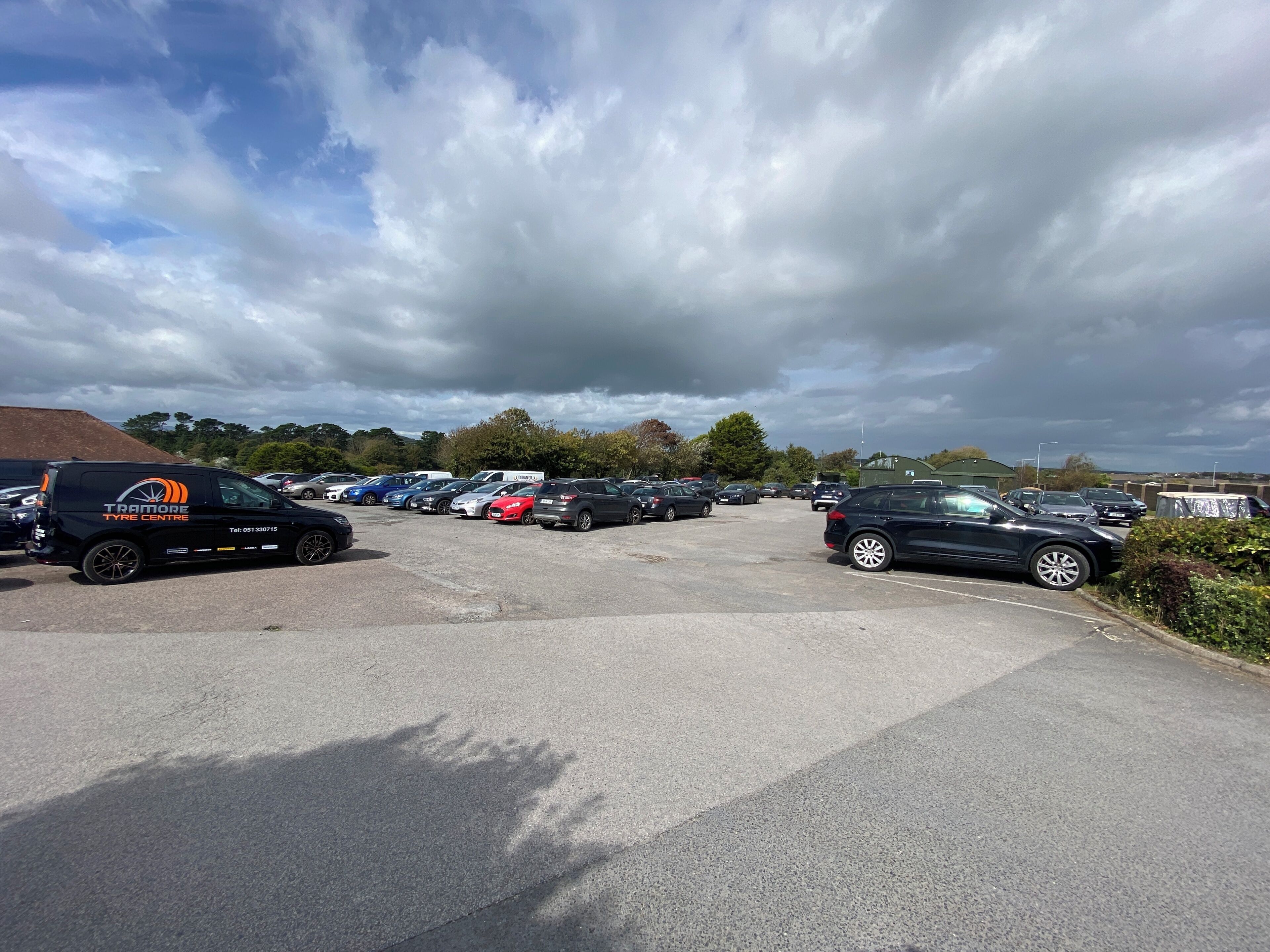 A parking lot with multiple cars and a black van with 'TRAMORE TYRE CENTRE' on the side.