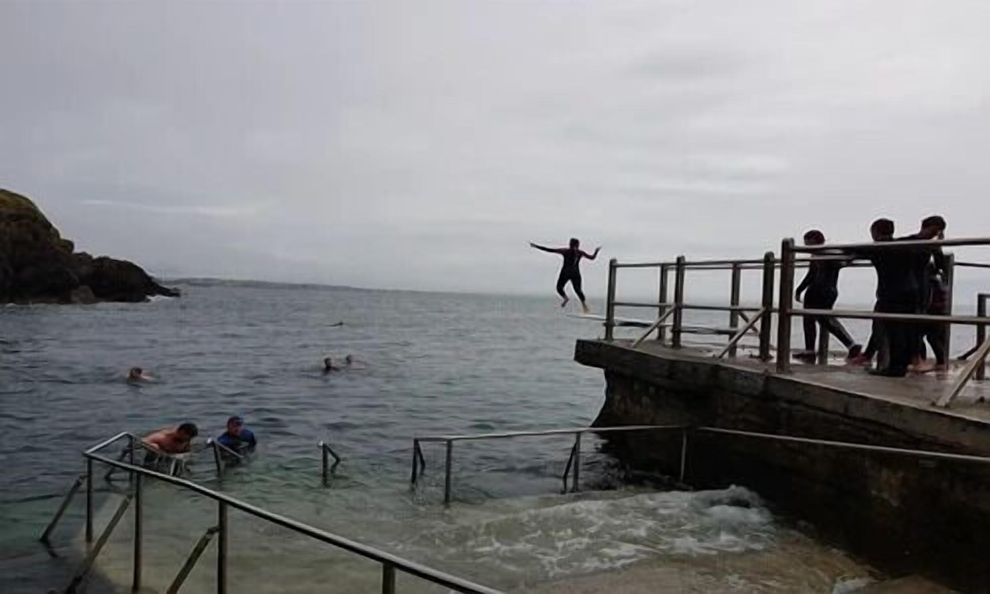 A pier with people swimming and jumping into the water.