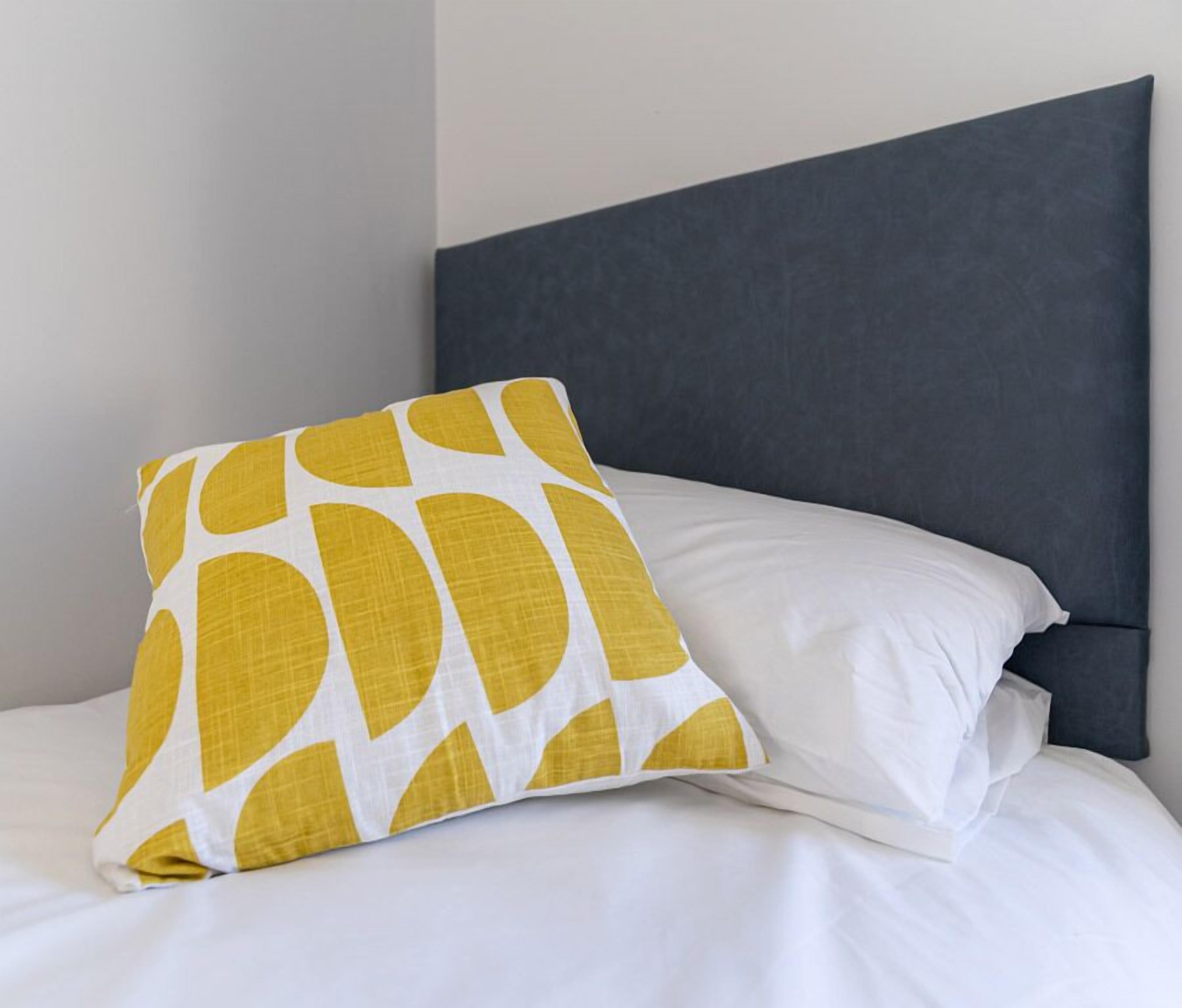 A bed with white bedding and a single yellow pillow with a white pattern.