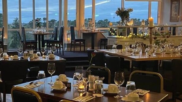 Un comedor con mesas dispuestas para el servicio, amplias ventanas que ofrecen vistas al exterior y un ambiente cálido y acogedor.