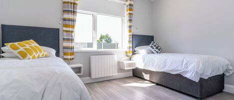 Une chambre moderne avec deux lits, une fenêtre avec des rideaux, un radiateur et une vue sur l’extérieur.