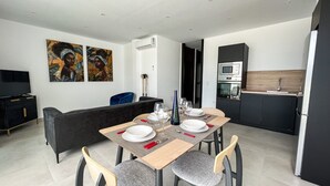 Un comedor moderno con una mesa dispuesta para cuatro personas, un sofá negro y una cocina al fondo.