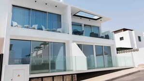 Un edificio moderno de dos plantas con amplios ventanales, techo plano y un balcón con mobiliario exterior.