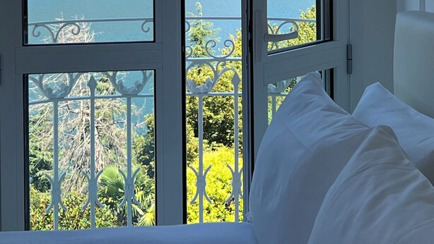 Ein Zimmer mit großem Fenster mit Blick auf eine gebirgige Landschaft und ein Gewässer.