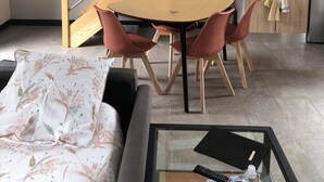 Una sala de estar moderna con un sofá, una mesa redonda y sillas. Una escalera con barandilla de madera conduce a un nivel superior.