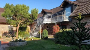 Una casa de dos pisos con balcón, fachada de ladrillo y un jardín cuidado con diversas plantas y un objeto esférico blanco.