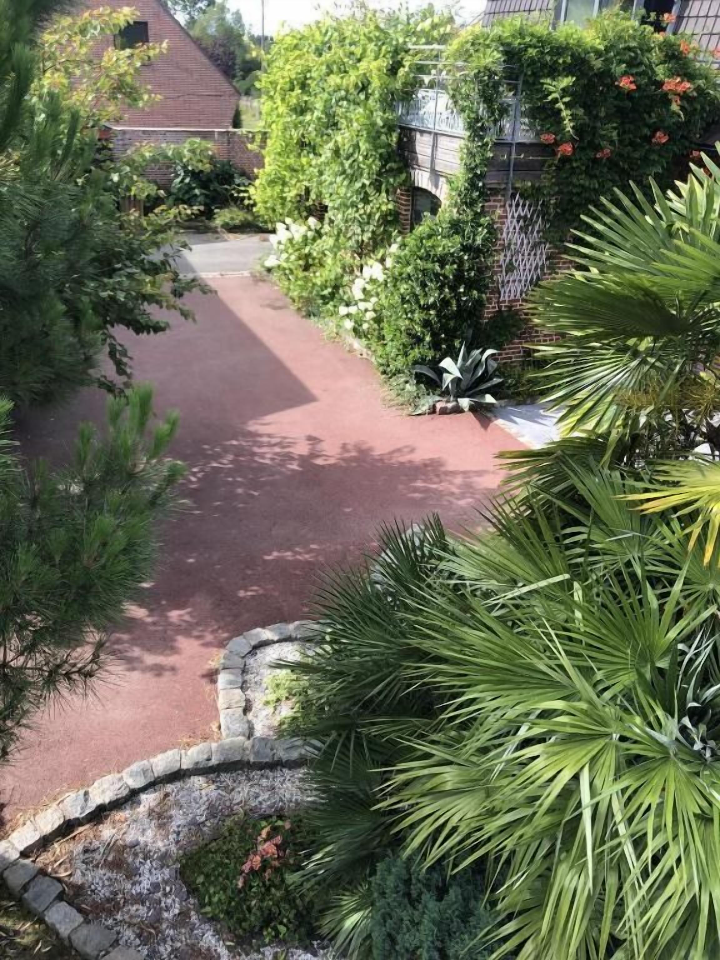 Ein gepflasterter Weg, umgeben von üppiger Bepflanzung und einem Backsteinhaus.