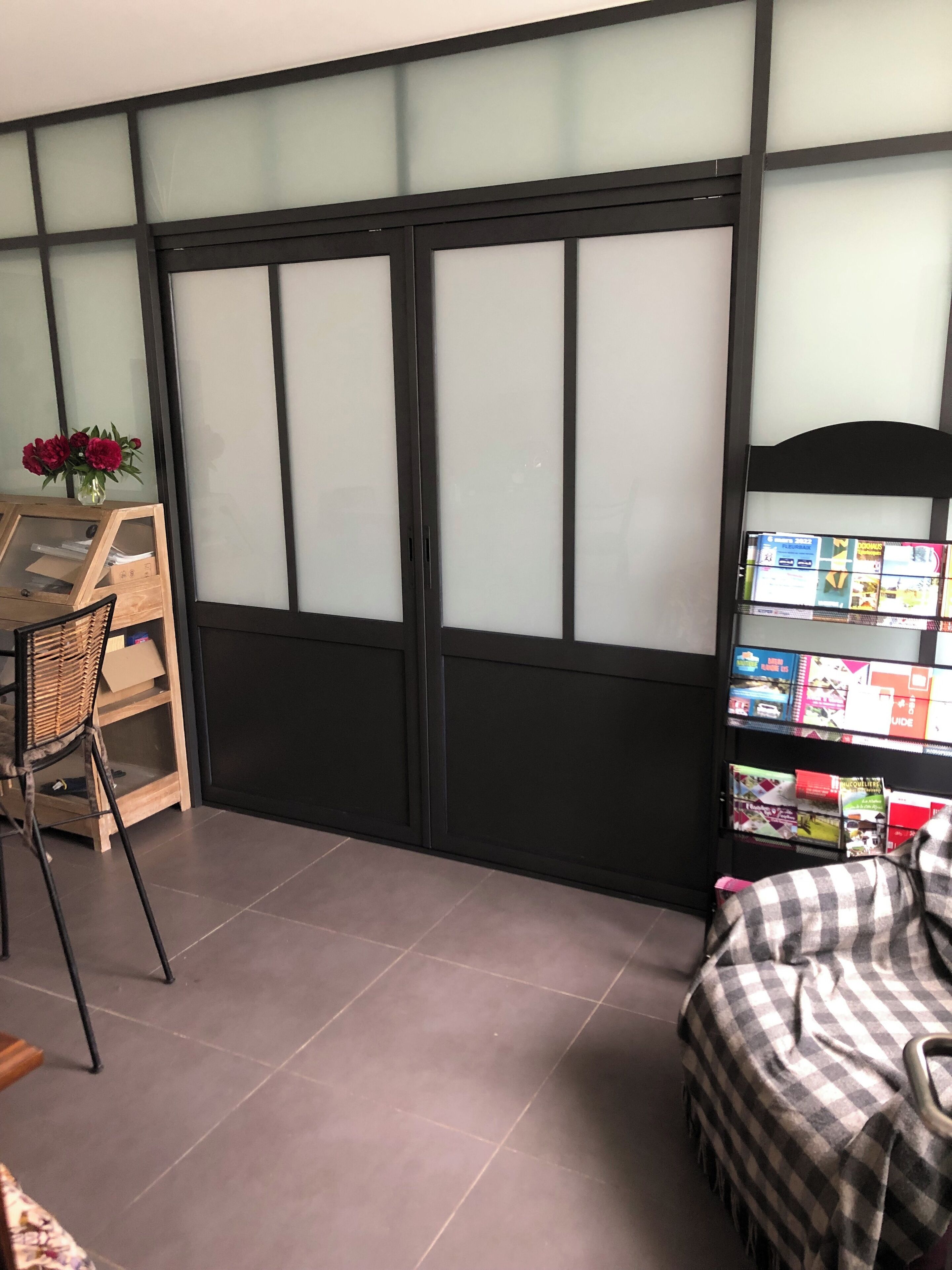 A room with a sliding door, a small table with a chair, a bookshelf, and a checkered blanket on a sofa.