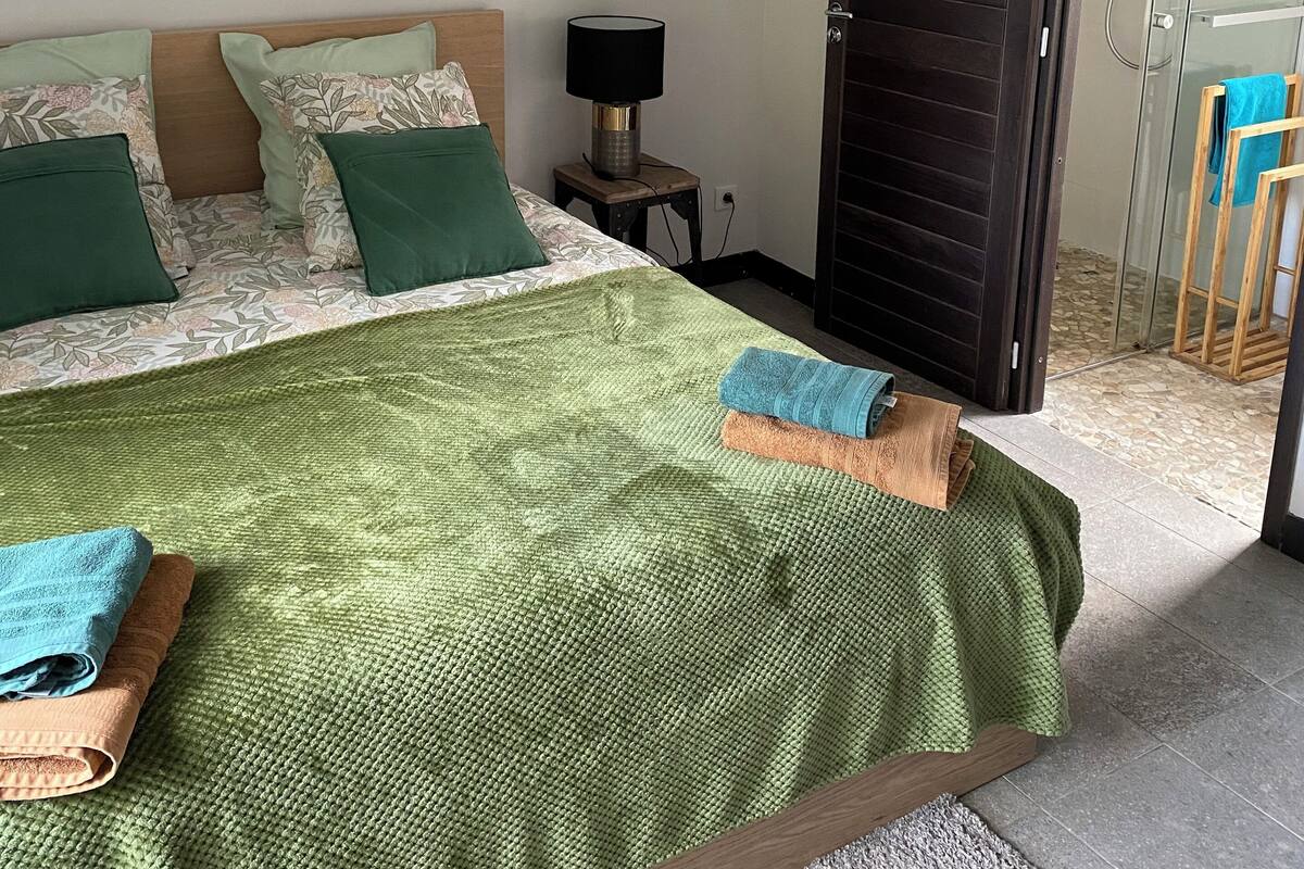 Un dormitorio con cama, almohadas, una mesita de noche, lámpara y puerta que da a un balcón.