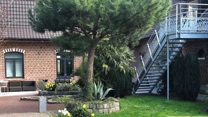 Un edificio de ladrillo con una escalera, un jardín con flores y un árbol, y un patio.