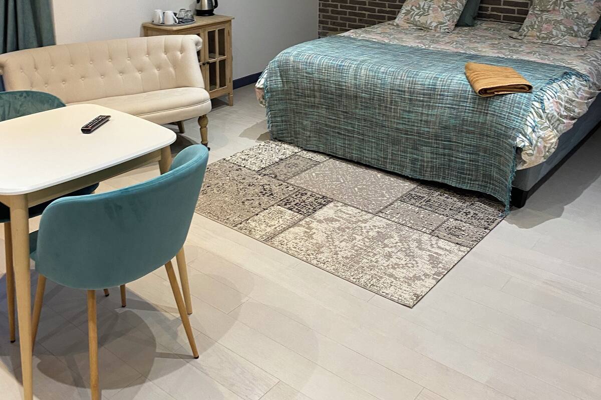Un dormitorio con una cama grande, un escritorio y una silla. Hay una mesita con una tetera y tazas, y un cuadro en la pared.