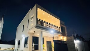 Una casa moderna de dos pisos con balcón, ventanas amplias y una entrada bien iluminada.