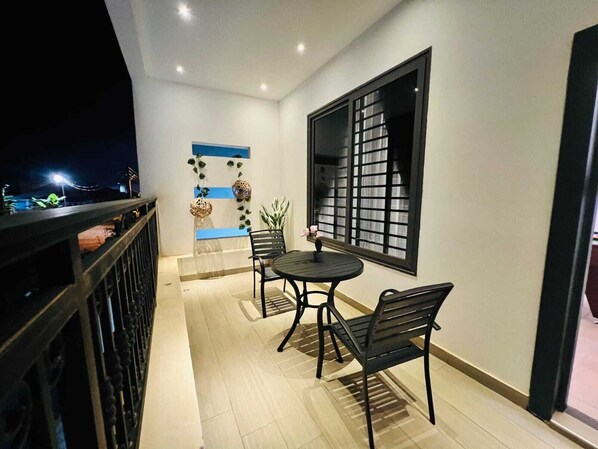Un balcón con mesa y sillas, un muro decorativo y una ventana con diseño de cuadrícula.