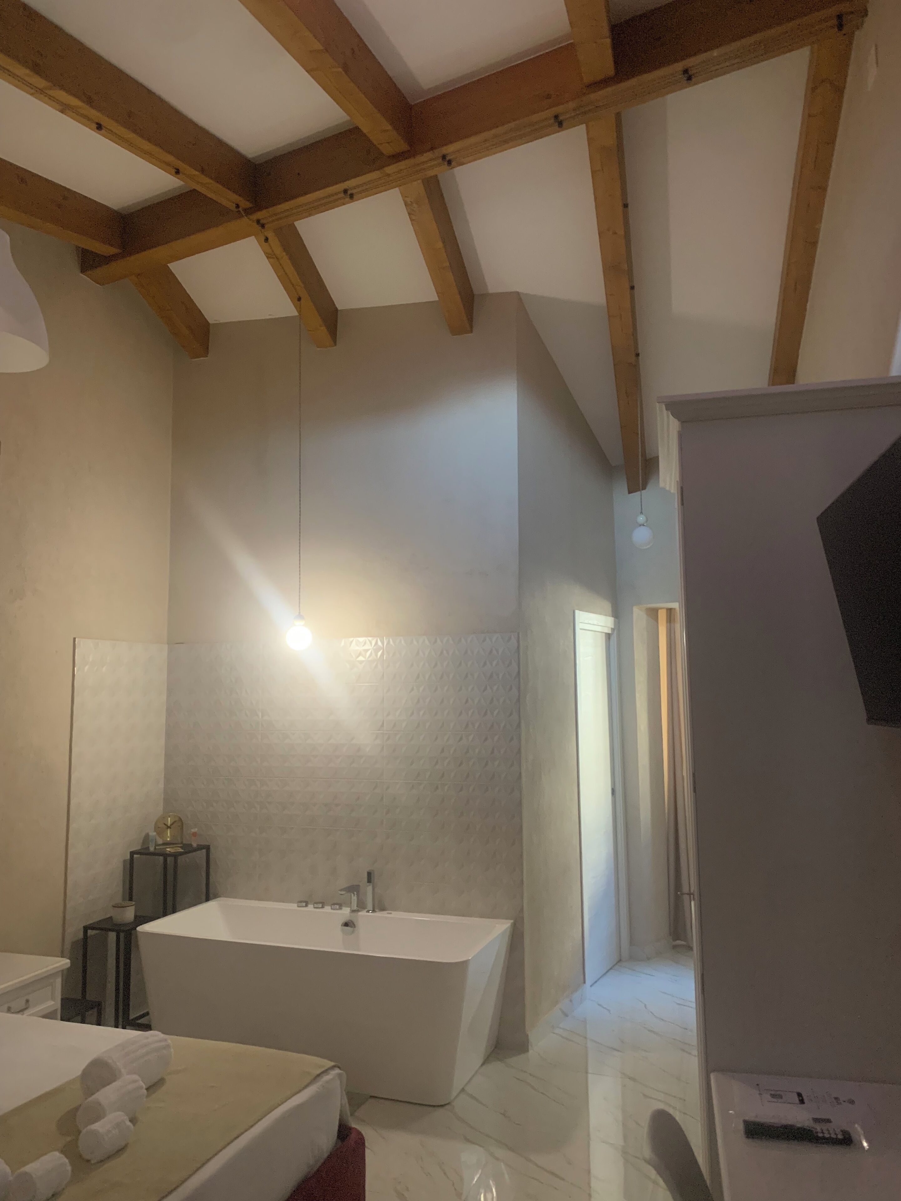 A modern bathroom with a freestanding bathtub, a large mirror, and a wooden ceiling.