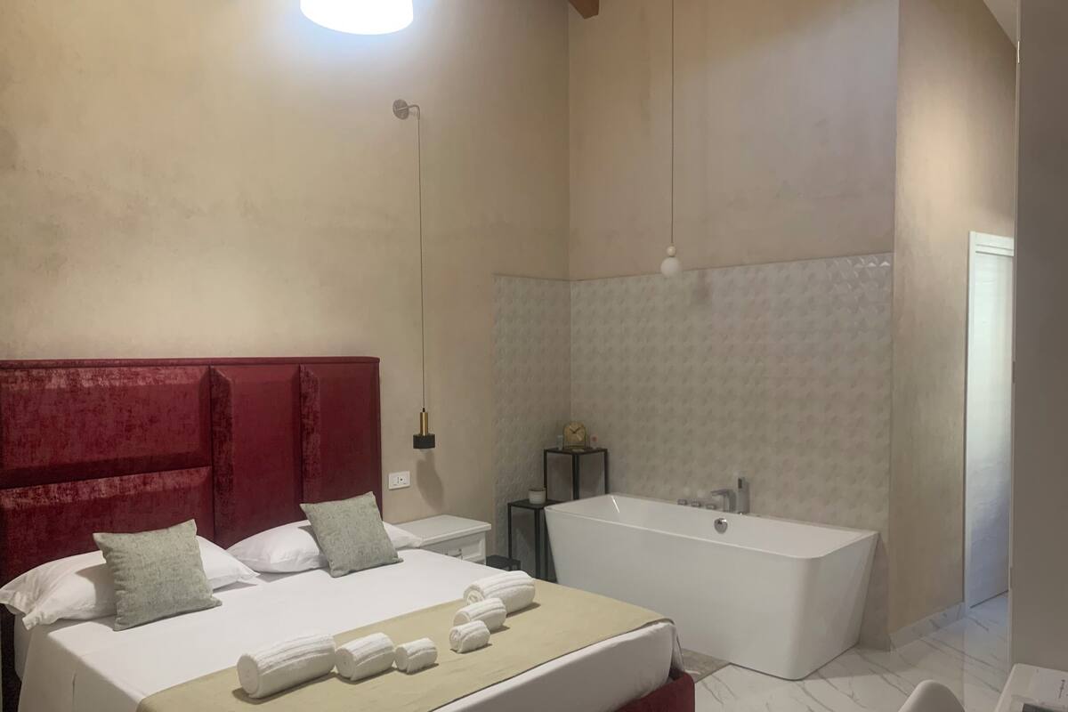 Une chambre moderne avec un grand lit, une tête de lit rouge et une salle de bain séparée avec une baignoire.