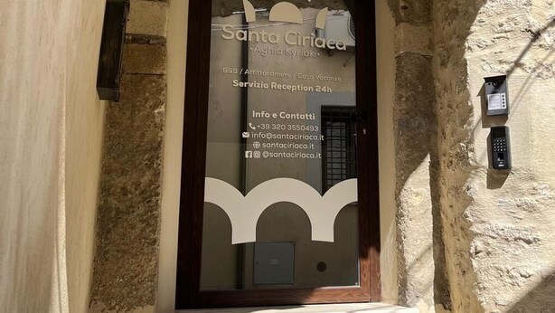 An arched doorway with a glass panel displaying the name 'Santa Ciriaee' and contact information. - Santa Ciriaca - Aghìa Kyriaki (Gerace)