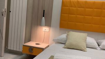 Ein modernes Hotelzimmer mit Bett, Nachttisch, Lampe und Heizkörper.